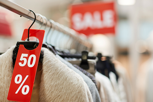 Background image of autumn clothes with red SALE tag on rack during Black Friday, copy space