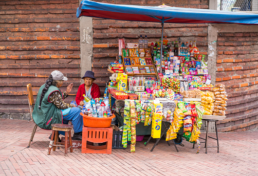 Quito, Ecuador - February 22, 2019: Two Woman selling sweets, drinks, crackers from kiosk on street in old historic part of Quite, Ecuador.  This is in the historical heart of Ecuador’s capital, a UNESCO World Heritage Site.