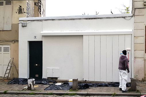 Paris, France - May 09, 2019: Man paints walls of facade house with white paint.