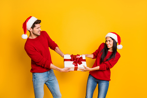 Profile side of angry couple pull package wear red sweater pullover santa claus cap denim jeans isolated over yellow background