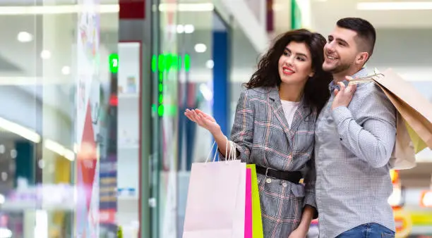 Woman showing new dress at shopwindow, shopping with husband in city mall, free space