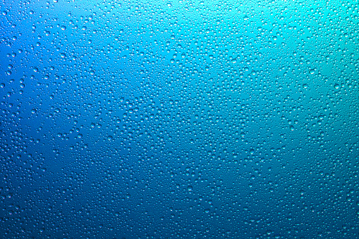 Sparkling water droplets on a translucent rainbow glass background with gradient color for a full frame texture or wallpaper