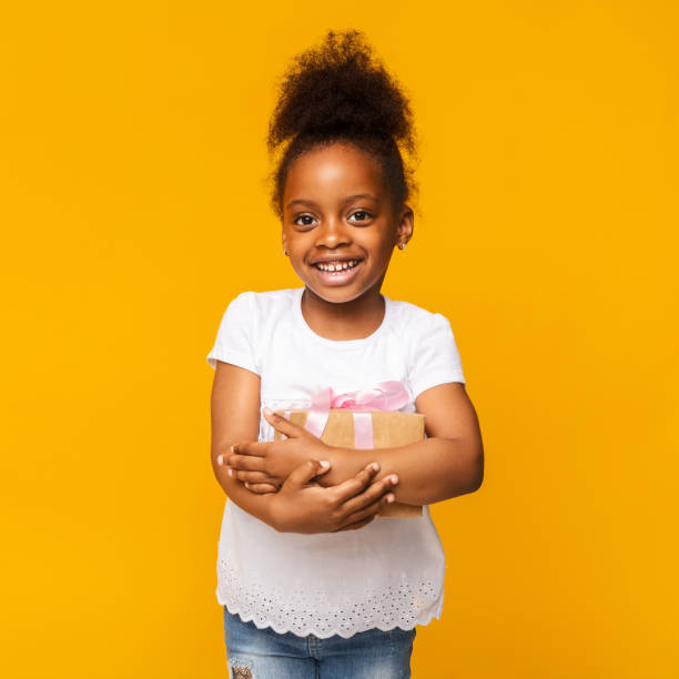 Lovely little african girl smiling with present box Lovely little african girl smiling with present box, orange studio background perfect gift stock pictures, royalty-free photos & images