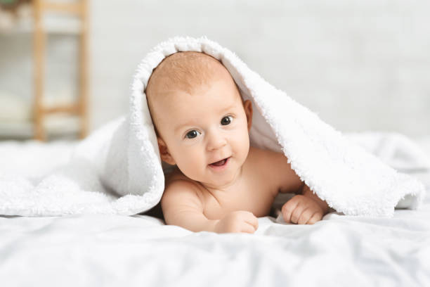 istock Adorable smiling baby boy lying on bed under white blanket 1176740073