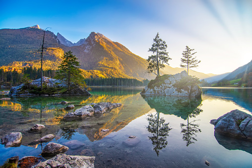 Majestic autumn sunset on Hintersee lake. Beautiful scene of trees on a rock islands, sunlit mountains reflected in the water. Berchtesgaden Alps, Bavaria, Germany