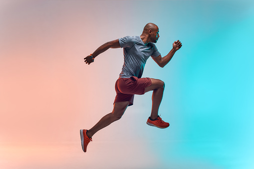 Nuevo campeón. Longitud completa de joven africano en ropa deportiva saltando sobre fondo colorido photo