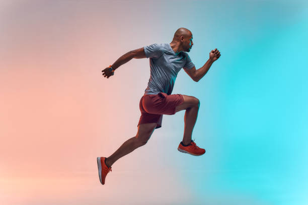 nuevo campeón. longitud completa de joven africano en ropa deportiva saltando sobre fondo colorido - saltar actividad física fotos fotografías e imágenes de stock