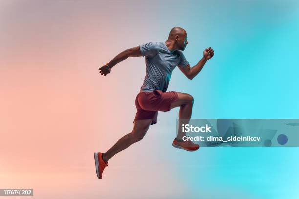 New Champion Full Length Of Young African Man In Sports Clothing Jumping Against Colorful Background Stock Photo - Download Image Now