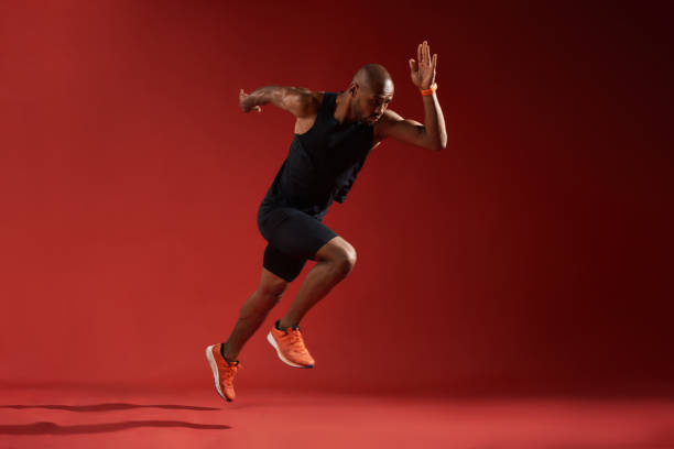 Never give up. Full length of young african man in sports clothing running in studio against red background stock photo