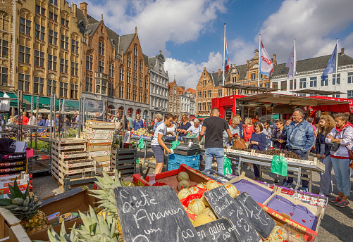 Fruit and Vegetable Market in Market Square of Bruges, Belgium. Local people are shopping from a farmer. Bruges, the capital of West Flanders in northwest Belgium, is distinguished by its canals, cobbled streets and medieval buildings.