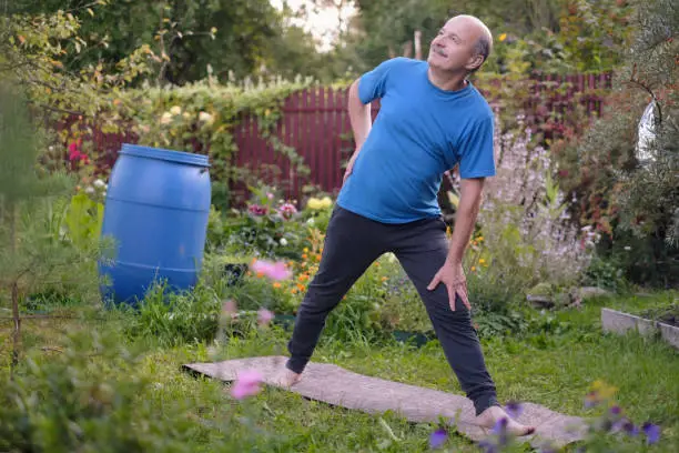 Senior hsipanic man   in garden, standing in Utthita Trikonasana, Extended Triangle Pose. Yoga for health at old age.