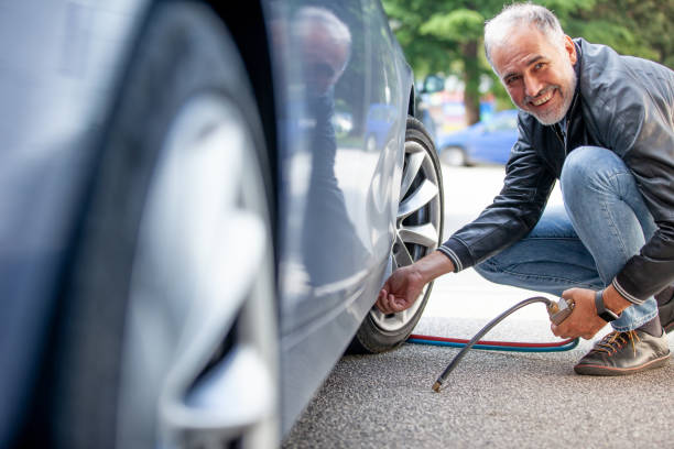 Smiling Mature Man Inflating Car Tires Outdoors Smiling Mature Man Inflating Car Tires Outdoors. inflating stock pictures, royalty-free photos & images