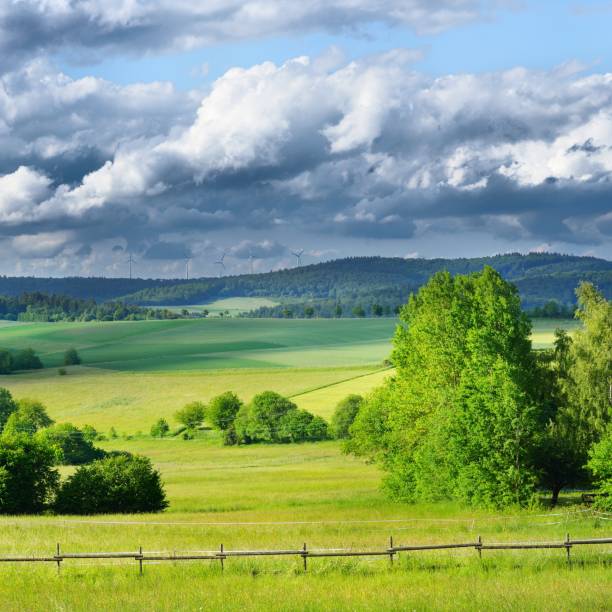 istock Green agricultural fields on hills with forest. Dramatic grey clouds in beautiful German countryside in Pfalz. Wind generators in the background. 1176754248