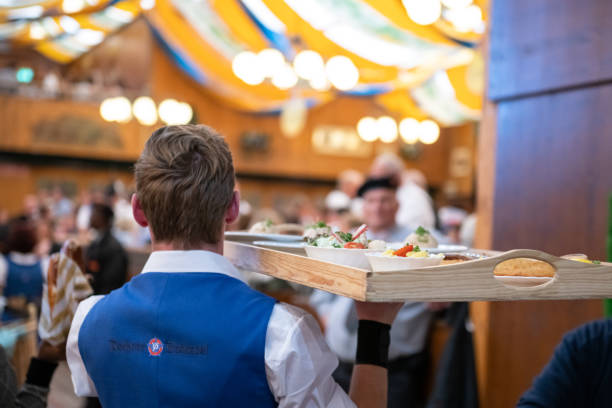 waiter carrying tray with food for the guest of Oktoberfest Munich, Germany - September 21, 2019: rear view on waiter  carrying wooden tray with traditional dishes for serving  to the guest of Oktoberfest oktoberfest food stock pictures, royalty-free photos & images