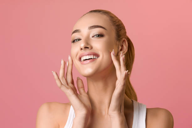 Portrait of beautiful woman touching skin or applying cream Portrait of beautiful woman touching skin or applying cream over pink background tooth in hand stock pictures, royalty-free photos & images