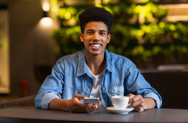 istock Cheerful black teen guy drinking coffee at cafeteria 1176757466