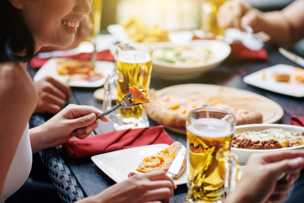 Close-up of young woman sitting at the table eating pizza and drinking beer together with her friends during lunch