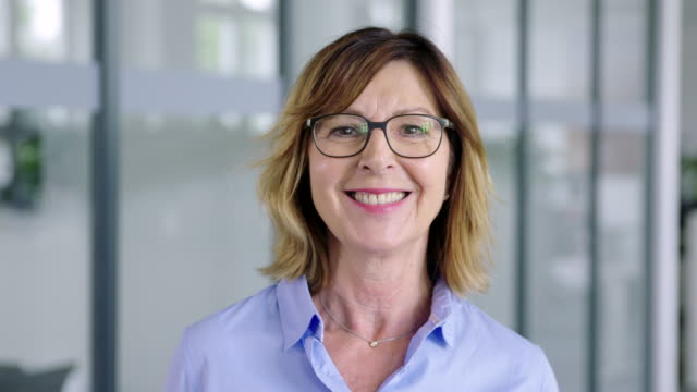 Close-up portrait of beautiful senior businesswoman with short blond hair wearing eyeglasses in office. Confident mid adult businesswoman in office.