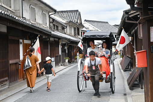 Okayama, Japan - September 16, 2019: A man is pulling rickshaw for tourists along the street in Kurashiki old town, Okayama, Japan
