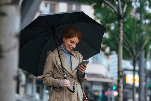 kobieta z parasolem stojącym na ulicy i wpisując telefon komórkowy - people in a row in a row business office worker zdjęcia i obrazy z banku zdjęć