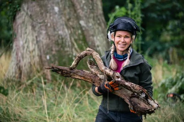 Woman wearing protective clothing smiling towards camera and holding firewood