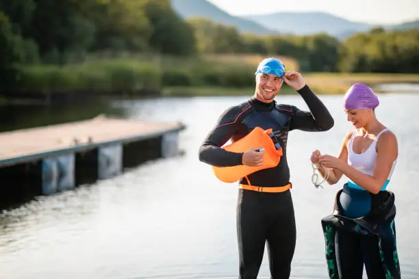 A young man and woman wearing swim caps and goggles preparing for a swim in Derwent Water in The Lake District in Cumbria