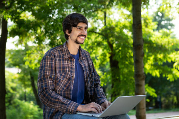 istock Young bearded brunet freelancer with mustache sitting with a laptop in a park. Work anywhere 1176780627