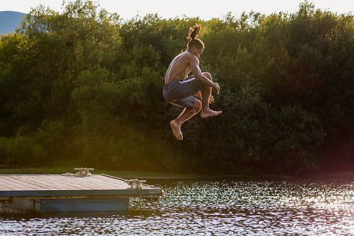 Young guy jumping off a jetty cannonball style into a lake in Derwent Water in Cumbria