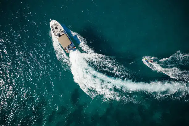 Aerial photo of man practicing wakeboarding towed by speed boat in deep blue sea