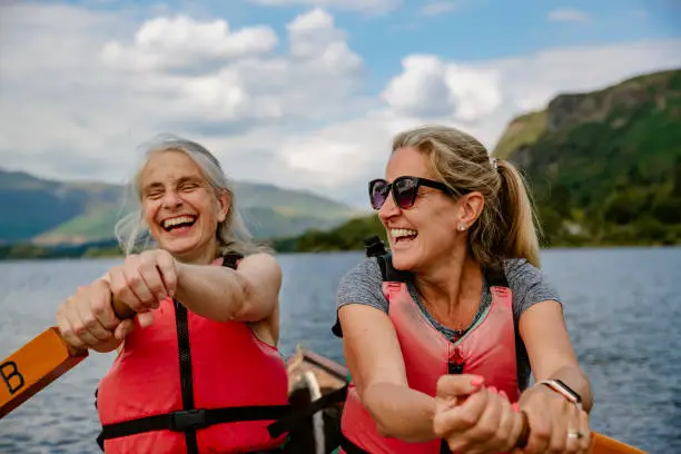 Two mature friends friends having fun in a rowing boat on Derwent Water in The Lakes District in Cumbria