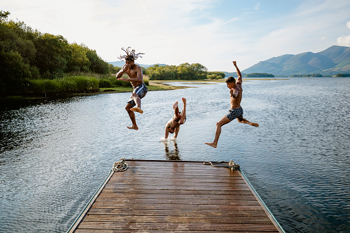 Young multi ethnic guys jumping off a jetty into a lake in Derwent Water in Cumbria