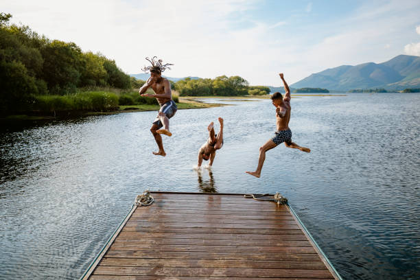 Dive Bomb Young multi ethnic guys jumping off a jetty into a lake in Derwent Water in Cumbria english lake district stock pictures, royalty-free photos & images