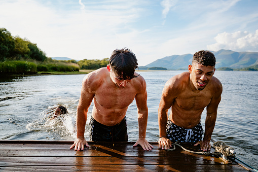 Young multi ethnic guys climbing out of the water on to a jetty in Derwent Water in Cumbria