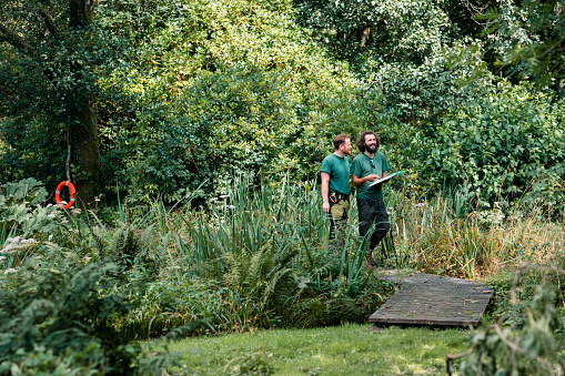 Two men looking at plants in lush garden and discussing with clipboard