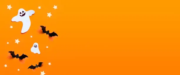 Photo of Autumn holiday composition. Halloween celebration concept with bats, ghost, spider web, stars over a orange background.