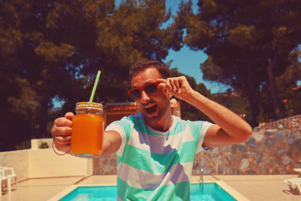 Attractive man drinking juice on the swimming pool. Summer concept.