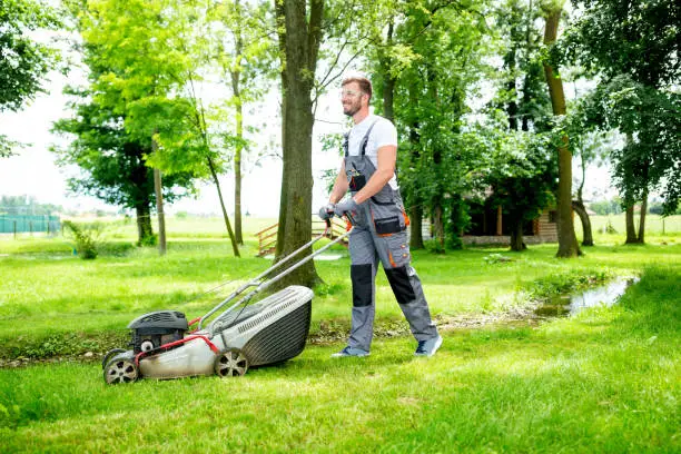 Gardener equipped with lawnmower on the job, concept of lawn mowing