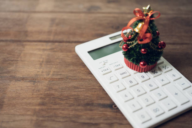 ein wunderschön geschmückter weihnachtsbaum platziert auf einem weißen rechner und mit einem miniatur-buch. weihnachten-konzept am 25 dezember jedes jahr gefeiert. - concepts calculator tax form finance stock-fotos und bilder
