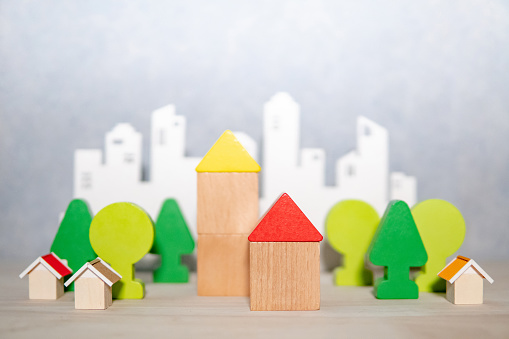 Group of wooden house and tree toy models with blurred city background on the table. Urban living concept