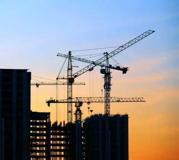 Photo of Crane and building silhouettes at blue yellow sky, sunset