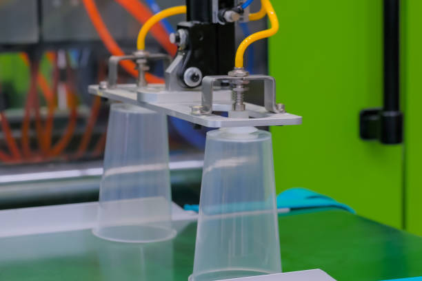 istock Cups on conveyor belt of plastic injection molding machine with robotic arm 1176810621