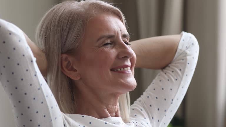 Happy dreamy older woman relax hands behind head at home