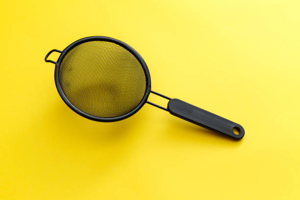 istock Black hand strainer isolated over a yellow background. 1176817295