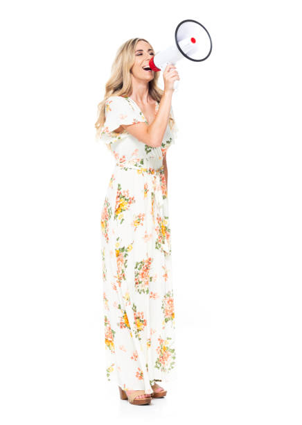 side view / profile view / full length of 20-29 years old adult blond hair / long hair caucasian young women standing in front of white background wearing dress / long dress and holding megaphone - 20 25 years profile female young adult imagens e fotografias de stock