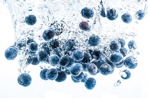 Fresh blueberries falling in water on white background. Fruits splashing into clear water. Antioxidant health concept