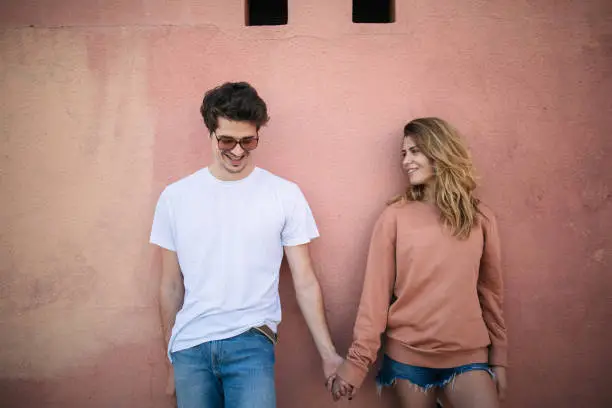 Photo of Teenage couple holding hands and leaning on wall.