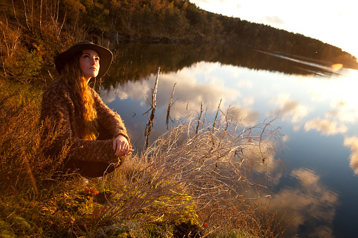 Beautiful young woman enjoying the autumn sun by a lake in Scandinavia.