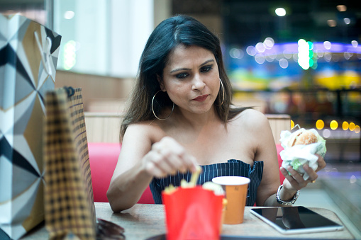 Fashionable woman drinking coffee and eating burger after shopping at modern mall