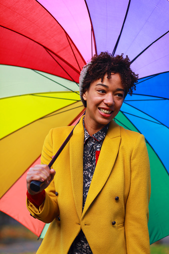 Young african-american woman holding a big rainbow colored umbrela. Happy and smiling autumn portrait.