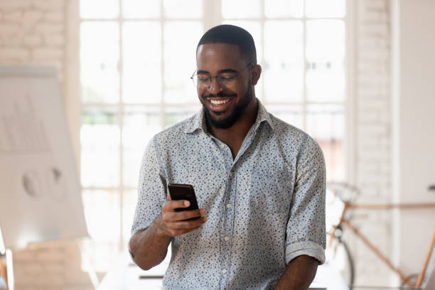 istock Happy black businessman holding smartphone using apps standing in office 1176842701